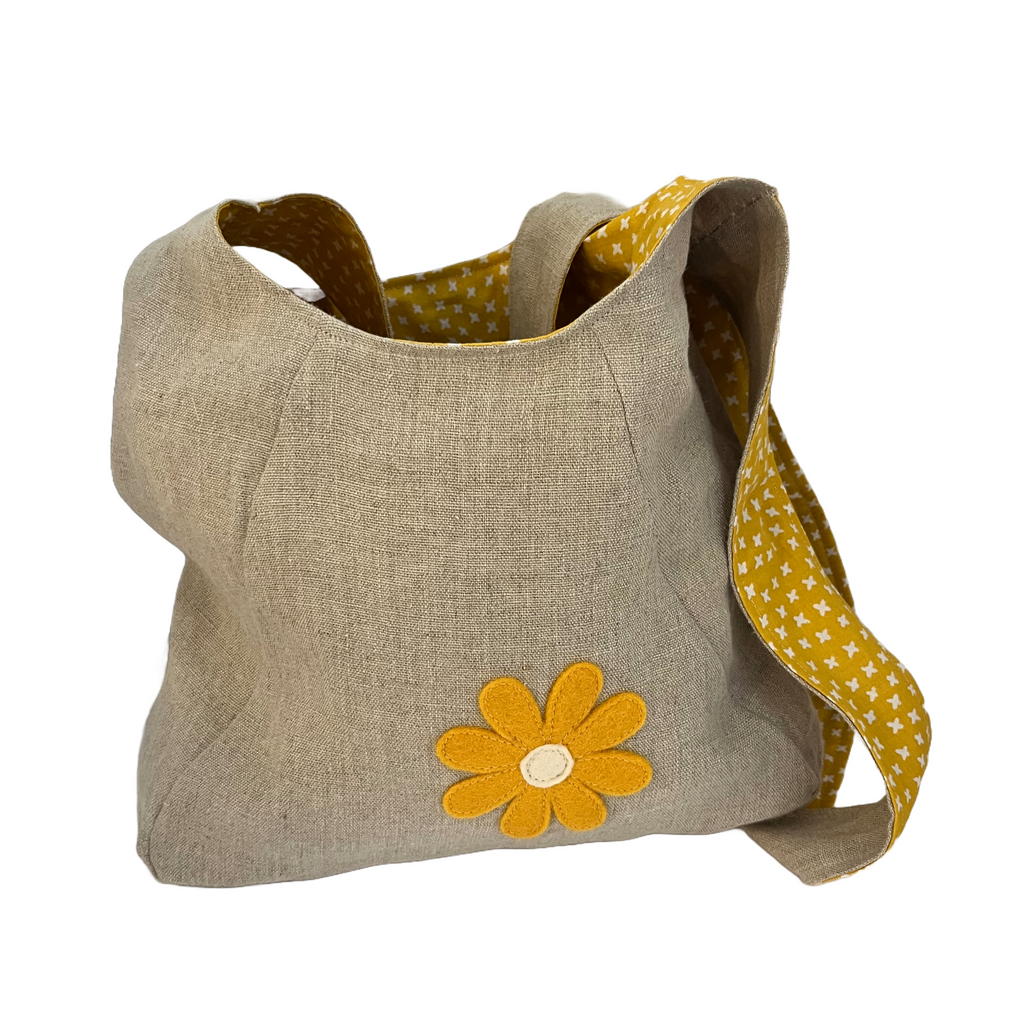 Beige bag with a yellow flower design and matching strap on a white background