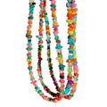A close-up of a hand holding three strands of colorful seed bead necklaces against a plain gray background.