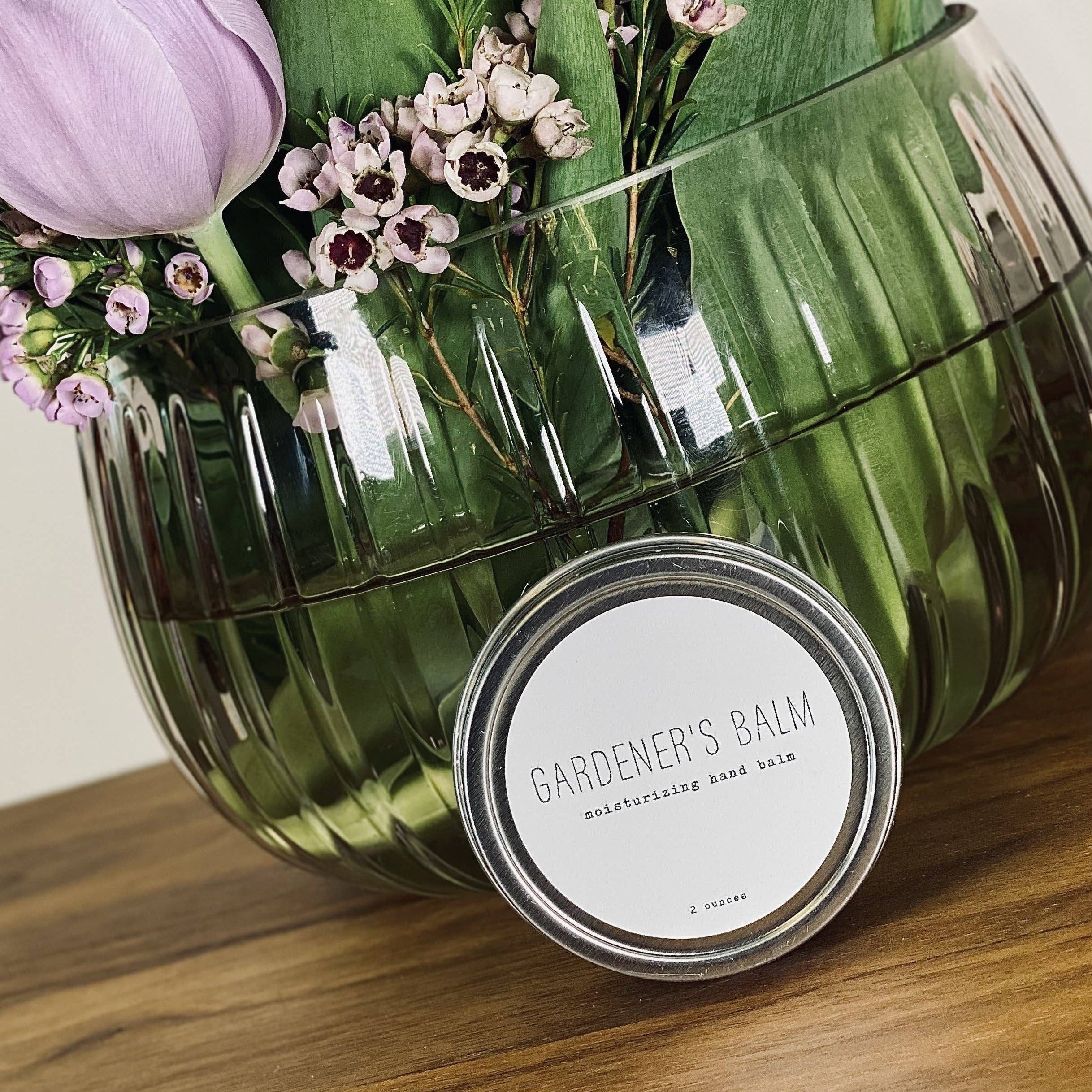 Glass vase with purple tulips and a jar labeled 'Gardener's Balm' on a wooden surface.