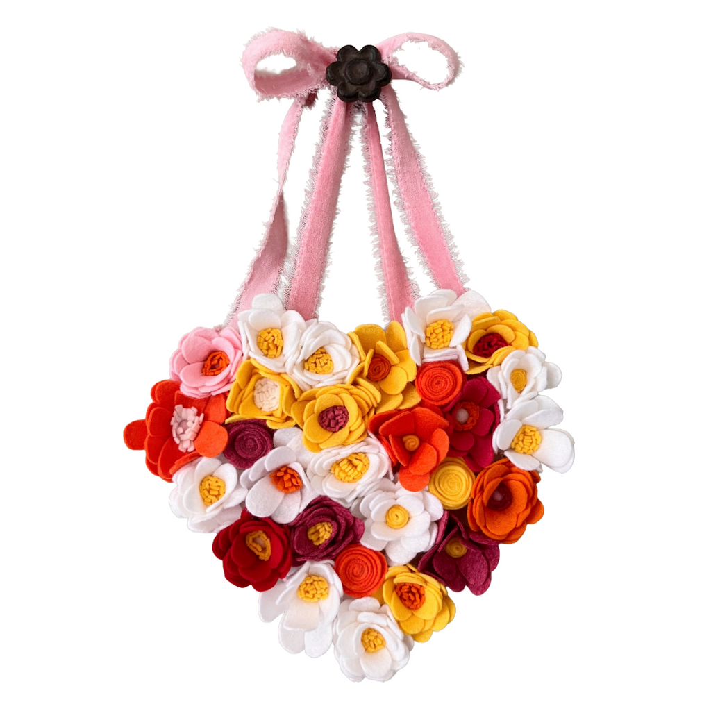 Heart-shaped flower arrangement with colorful flowers on a pink ribbon against a white background