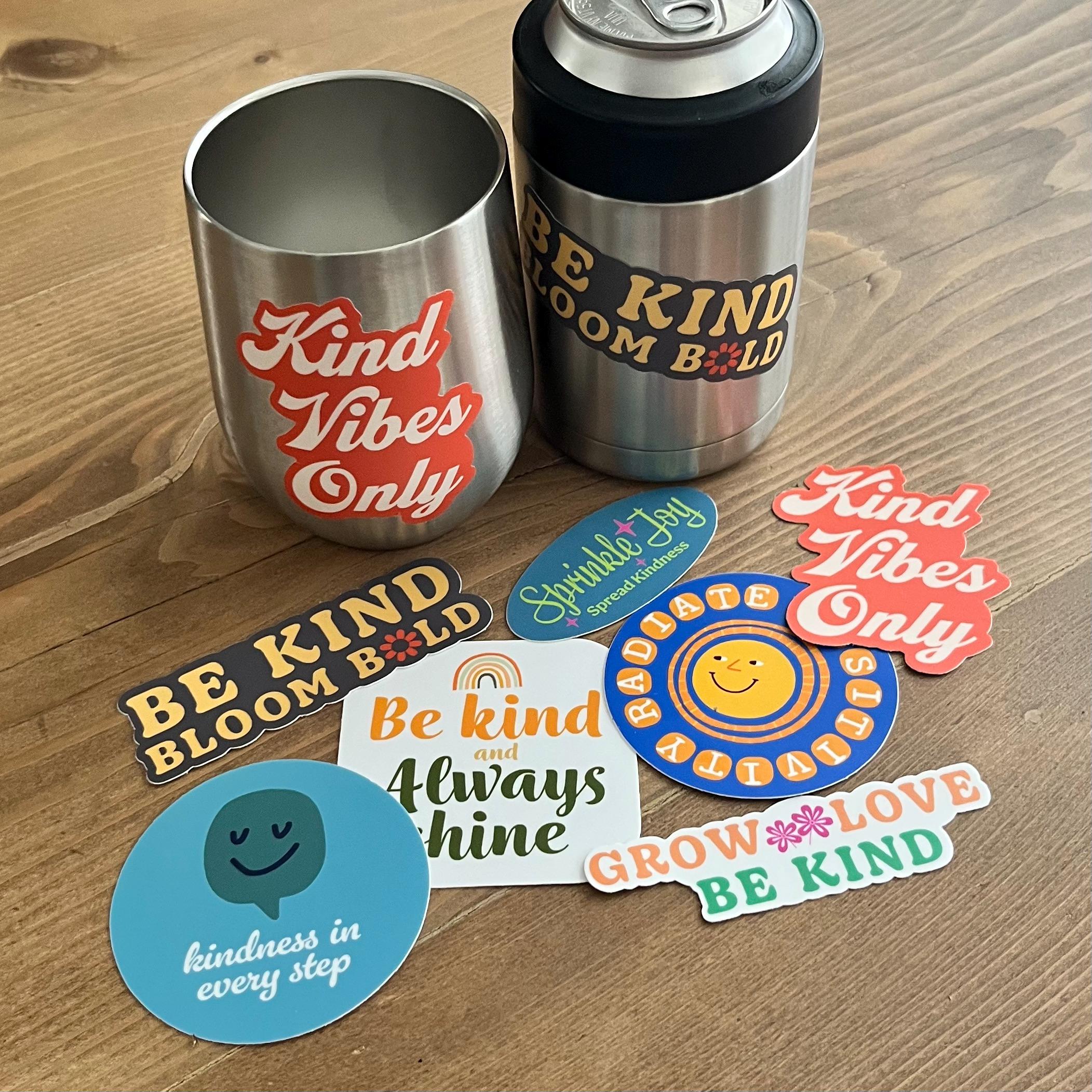 Two stainless steel tumblers with motivational text and stickers on a wooden surface.