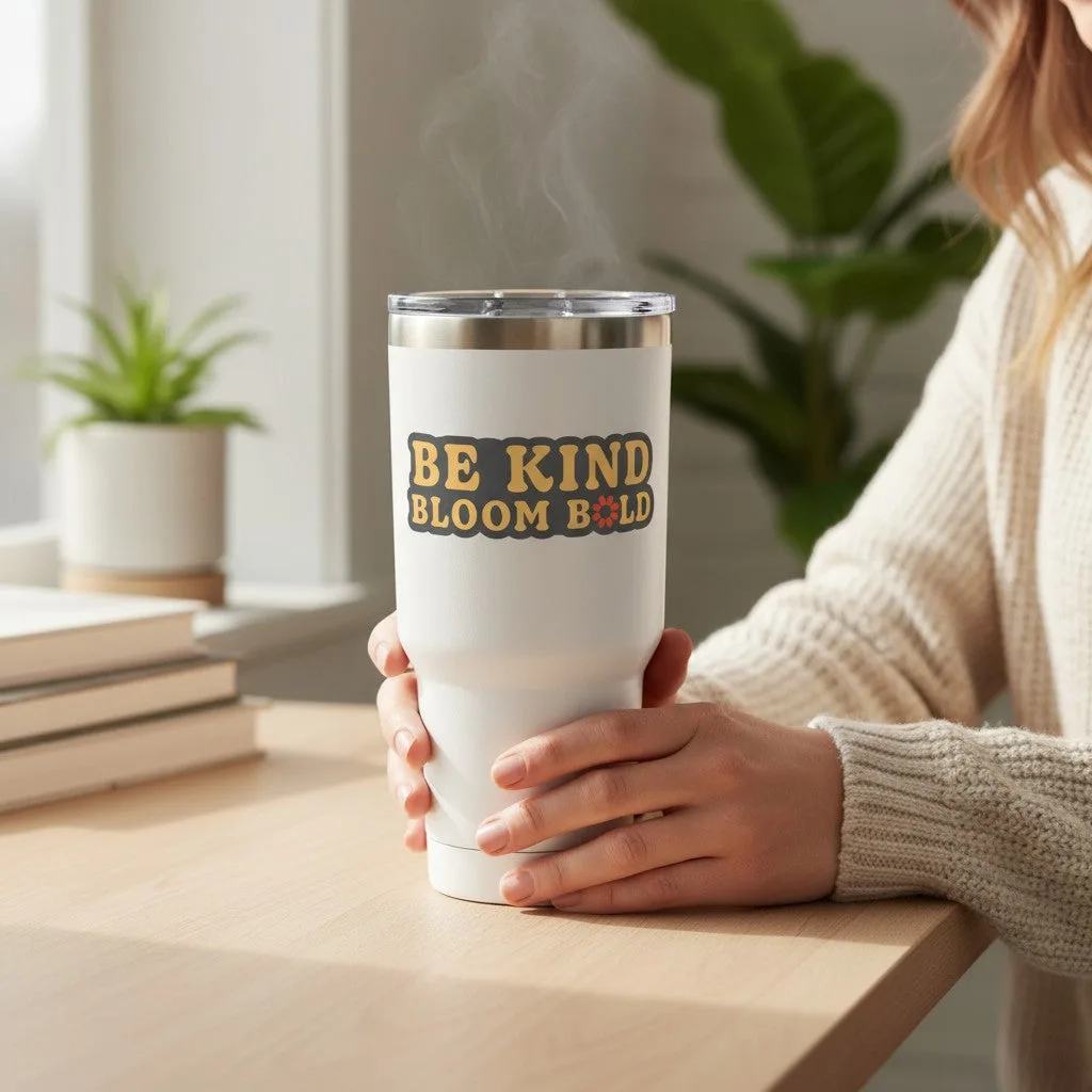 Be Kind Goods Be Kind Bloom Bold vinyl sticker on a white insulated tumbler held by a person in a cozy room