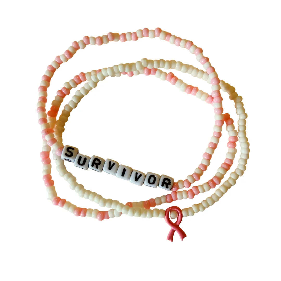 Beaded bracelets with alternating cream and pink beads, featuring white letter tiles spelling 'SURVIVOR' and a small pink awareness ribbon charm, shown on a plain white background.