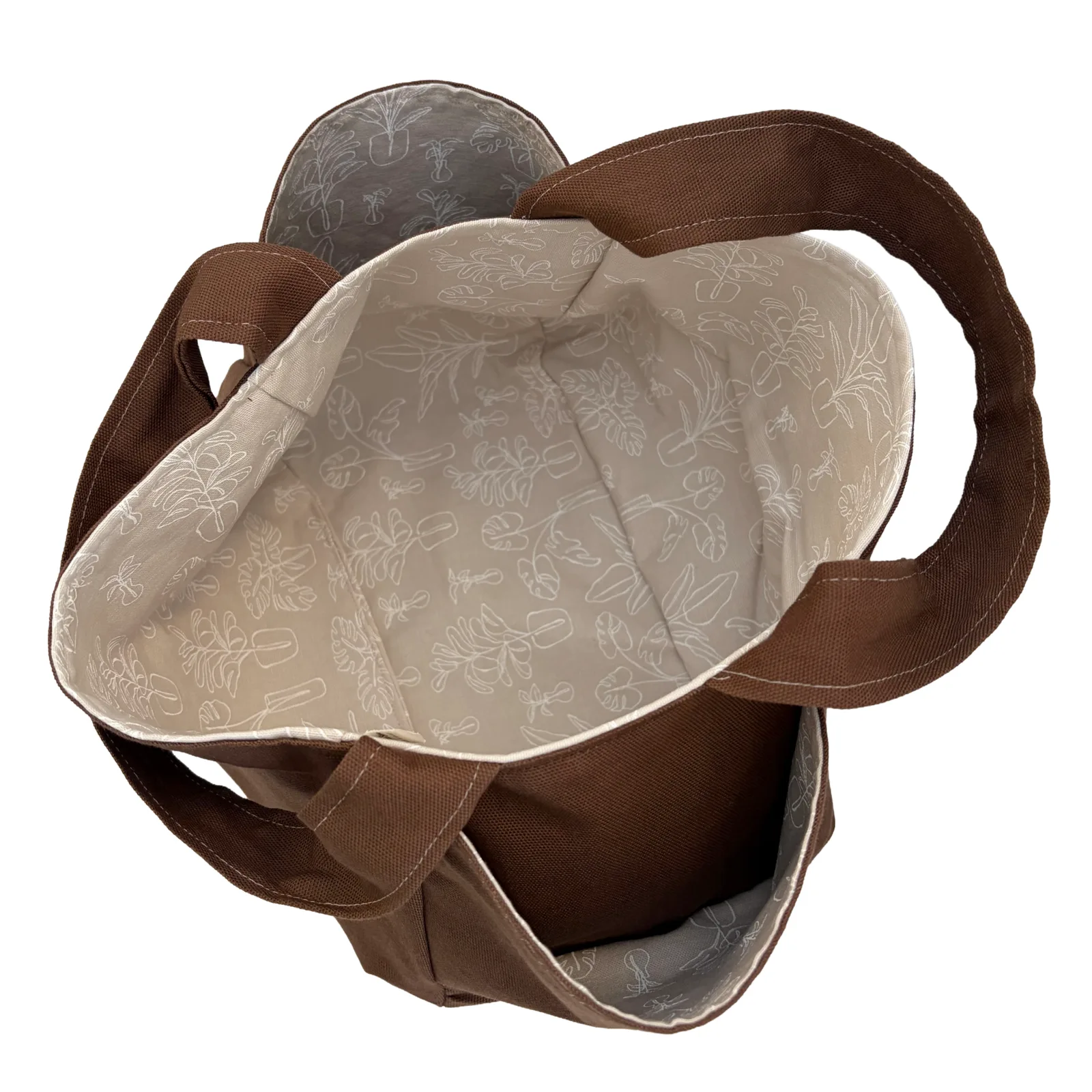 A brown canvas tote bag shown open from above, revealing a beige interior printed with a delicate white floral pattern.