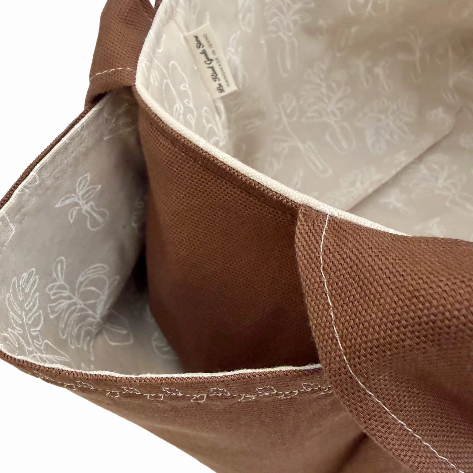 Close-up of the interior of a brown canvas tote bag with a light beige floral-patterned lining and white stitching.