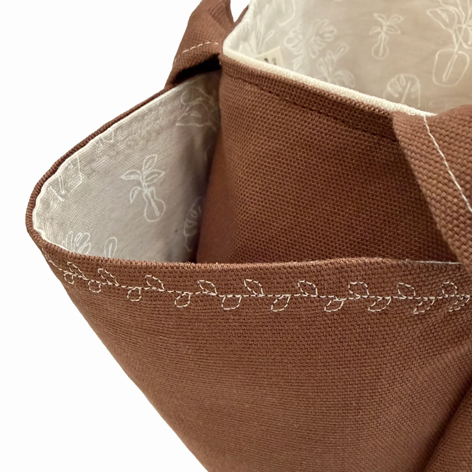 Close-up of a brown canvas tote bag showing the interior lining with a light beige floral pattern and white decorative stitching along the rim.