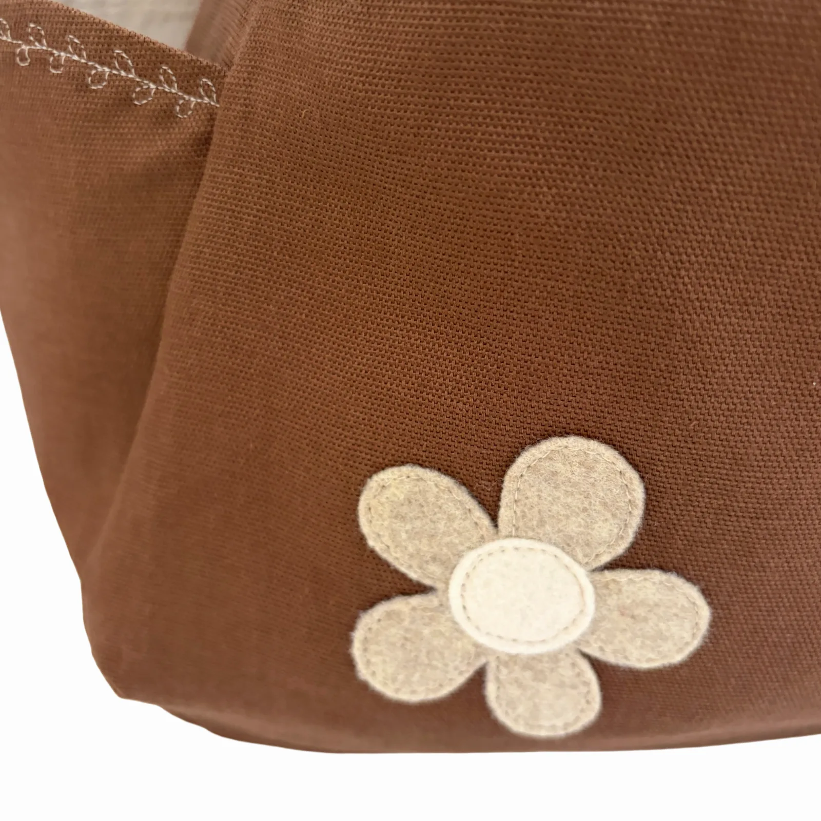 Close-up of a brown fabric bag with a beige felt flower applique on the front.