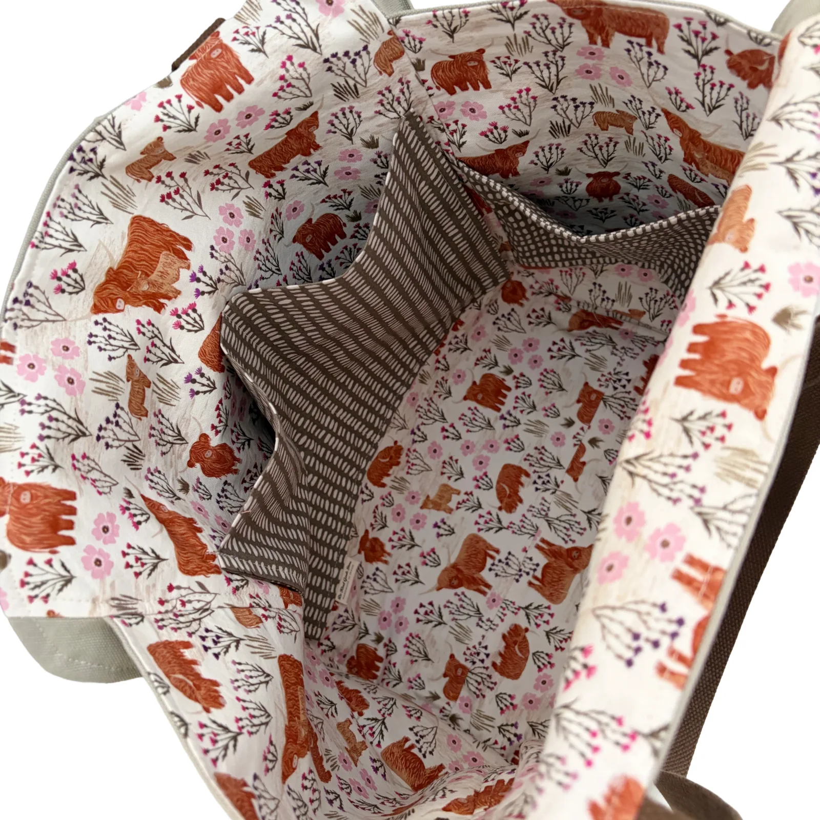 Close-up of the interior of a fabric tote bag, showing a printed lining with brown bears, pink flowers, and leafy motifs on a light background, plus a brown-and-white striped fabric pocket.