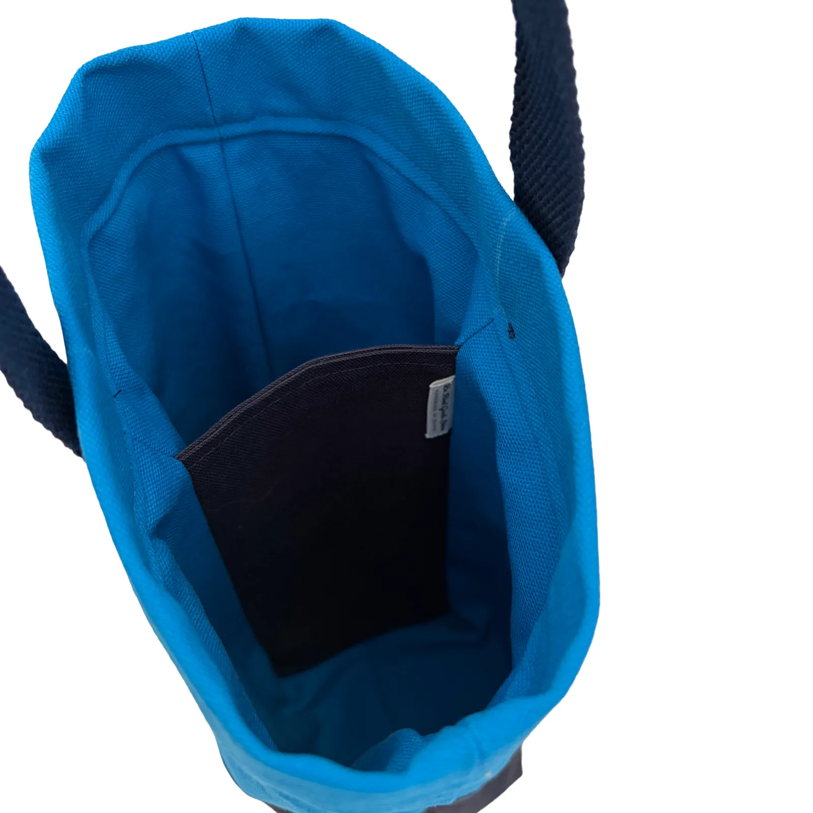 Close-up of the interior of a bright blue tote bag, showing a dark pocket lining and dark woven handles against a white background.