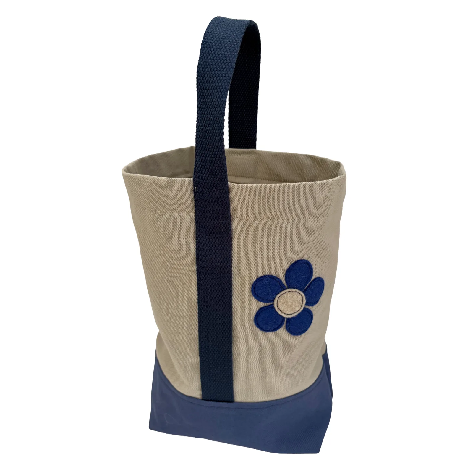 A canvas wine tote bag in beige and navy blue, featuring a vertical navy blue handle, a navy blue bottom panel, and a blue flower applique on the front.