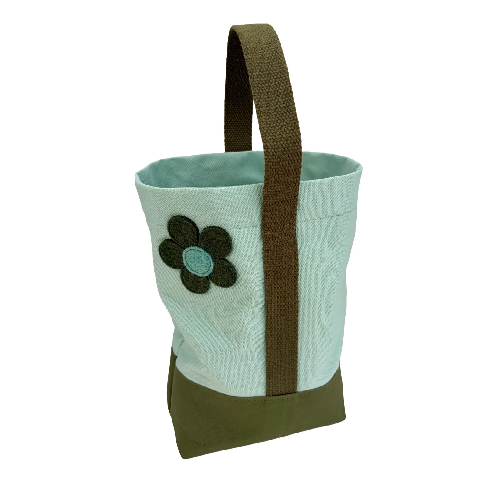 A canvas wine tote bag with a light mint green body, an olive green base, and an olive webbed handle. A dark green flower applique with a light blue center is stitched on the front.