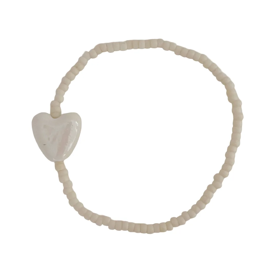 Cream beaded bracelet with a heart-shaped charm on a white background