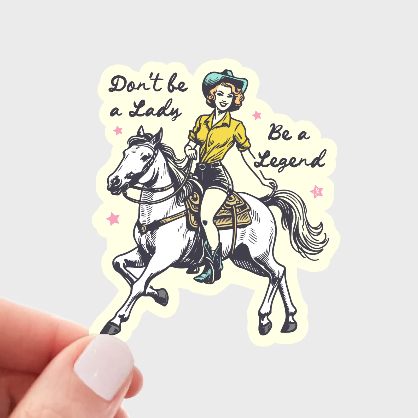Sticker with a woman riding a horse and text 'Don't be a lady, be a legend' held by a hand.