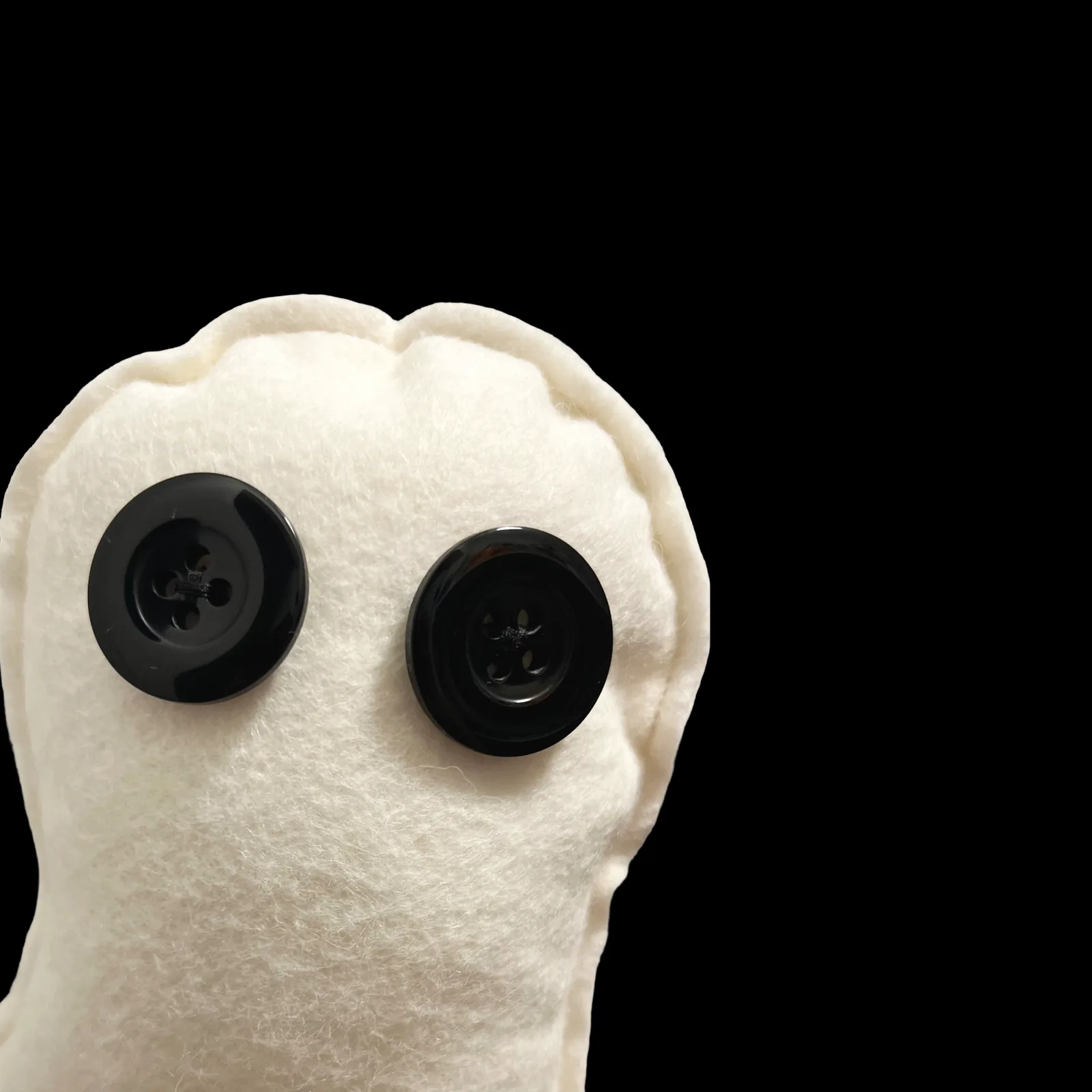 White felt ghost face with black buttons on a black background