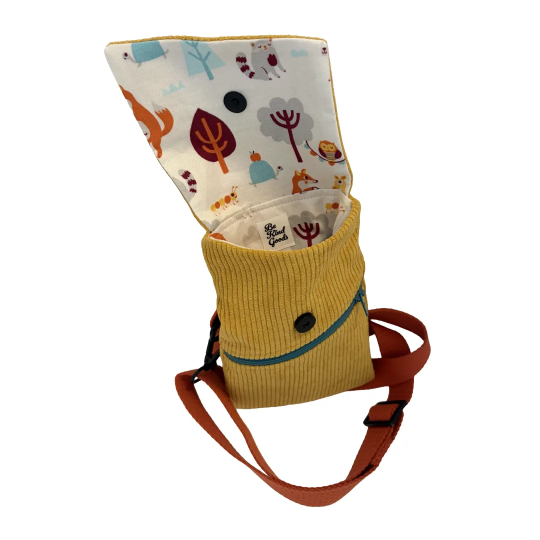 A mustard yellow corduroy pet carrier pouch with an orange-brown adjustable strap, featuring a woodland animal print lining on the inside flap.
