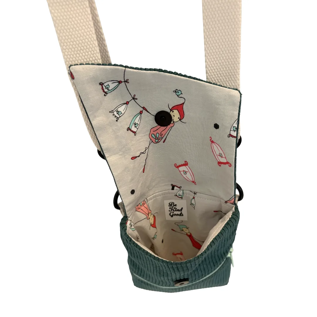 A close-up of a fabric accessory pouch with a cream-colored interior printed with whimsical fairy and lantern illustrations, a teal corduroy bottom, and a matching woven strap, shown against a plain white background.