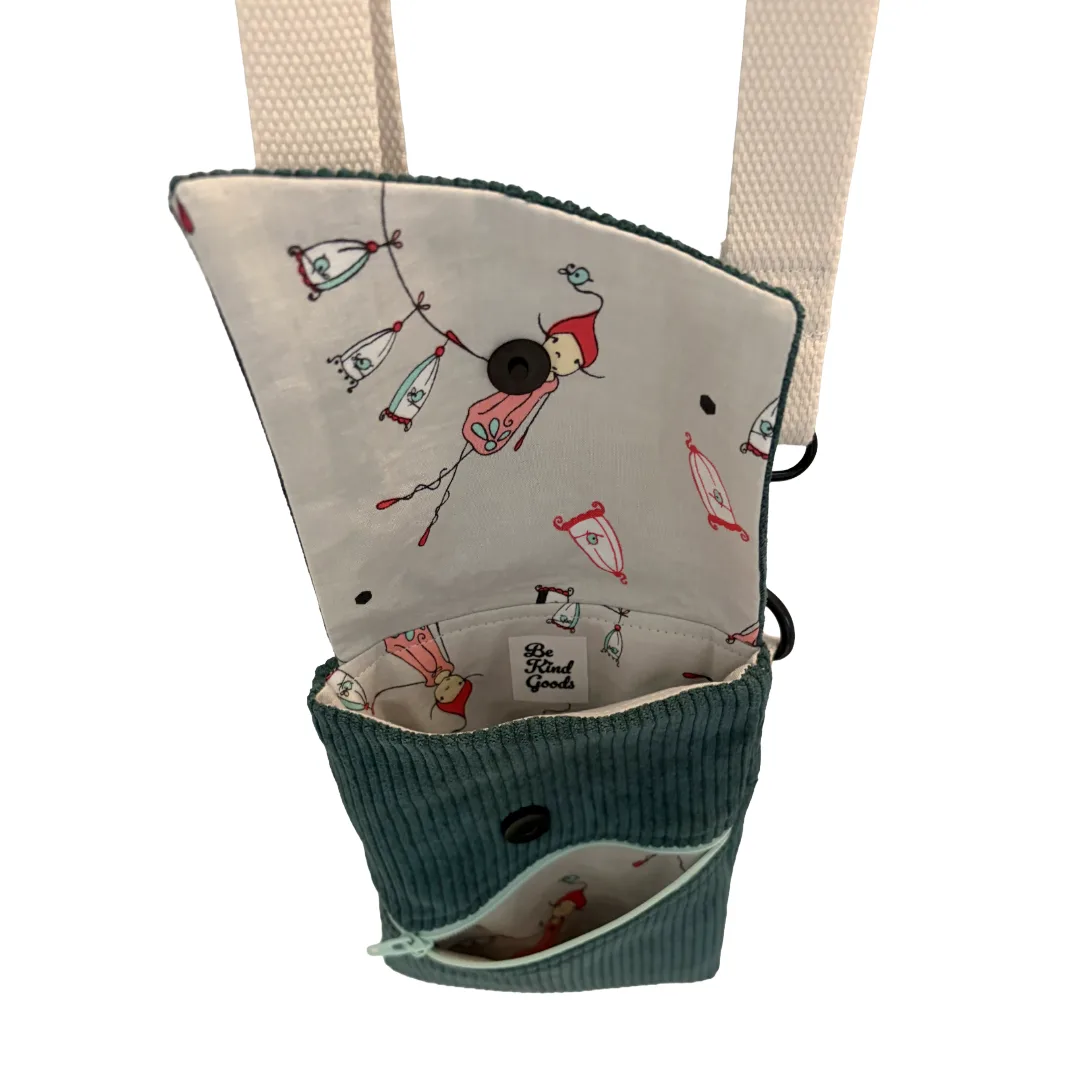 A small fabric accessory pouch with a teal corduroy exterior, cream interior, and a matching cream webbing strap. The pouch features a whimsical print of a girl in a red hat flying a kite, with a black button closure on the flap and a zippered pocket on the front.