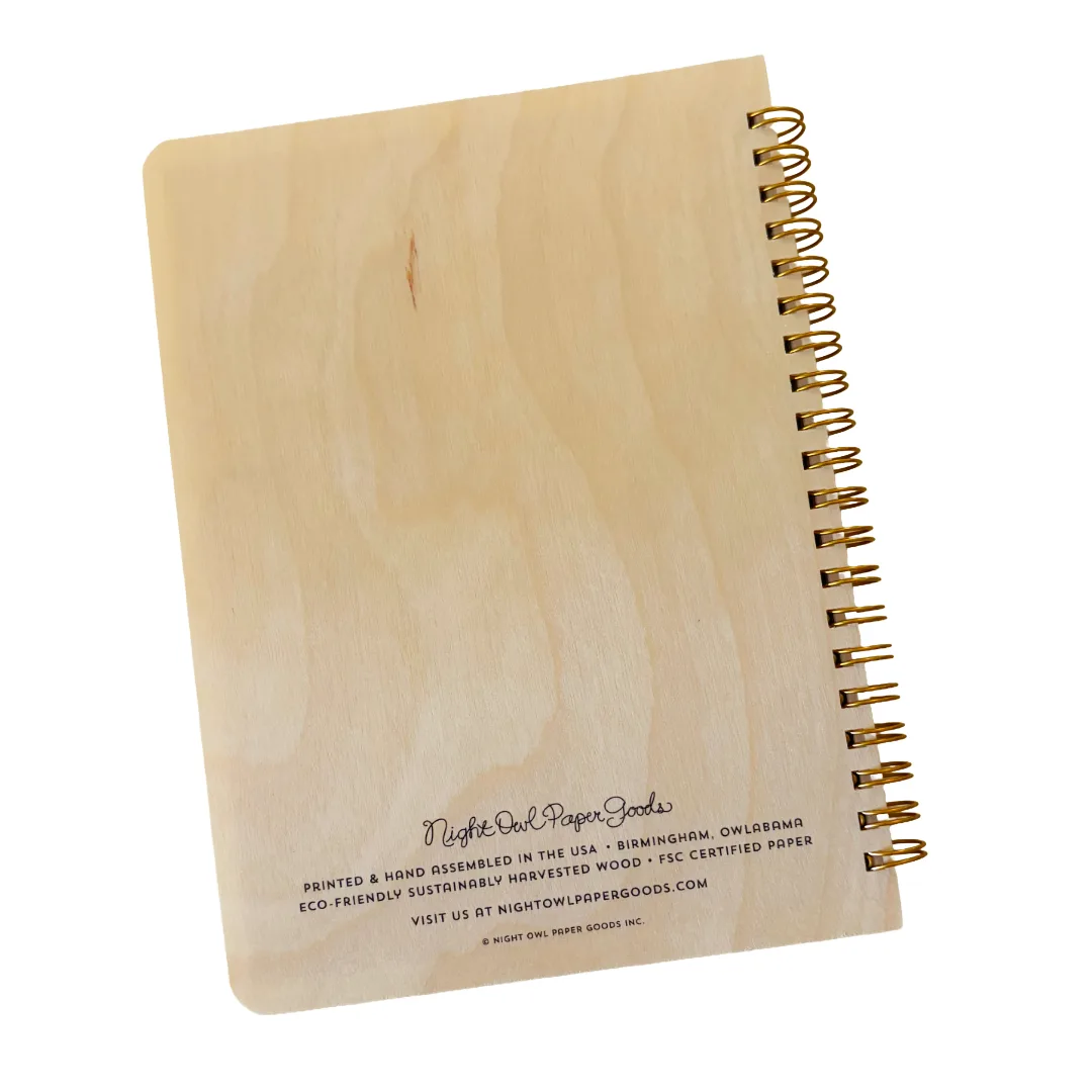 A spiral-bound notebook made from light natural wood with a gold-tone spiral binding, shown on a plain white background. The front cover has laser-etched text reading 'Night Owl Paper Goods' and smaller product details.