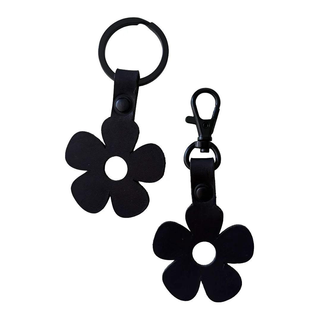 Two black flower-shaped keychains with five-petal cutouts, shown on a plain white background. One has a split key ring and the other has a lobster clasp, both attached to black strap sections with snap buttons.