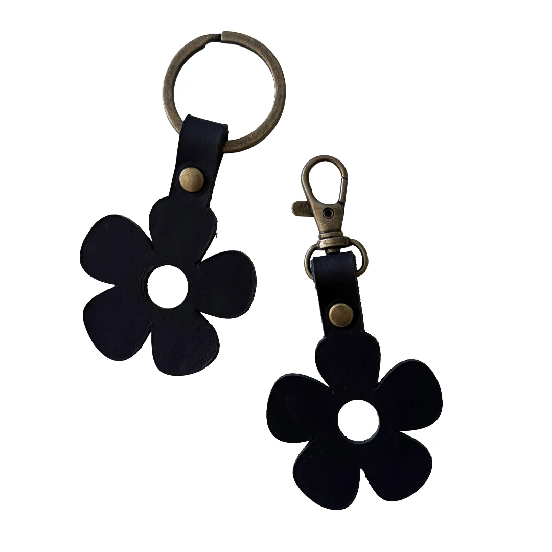 Two black flower-shaped keychains with brass key rings and clasps, displayed on a solid white background.