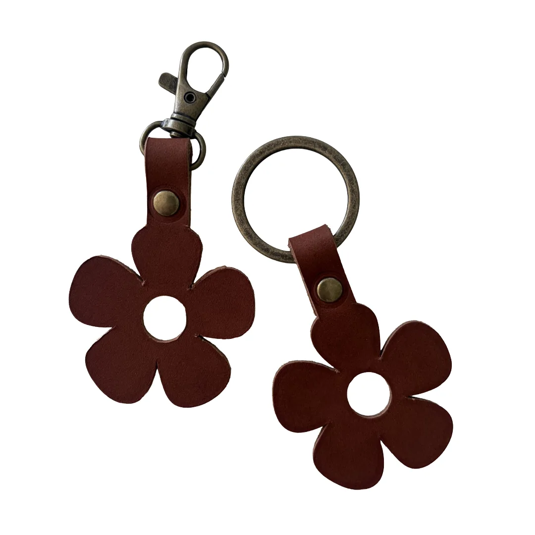 Two dark brown leather flower-shaped keychains with five petals, a center cutout, and a brass snap clasp, shown on a plain white background.