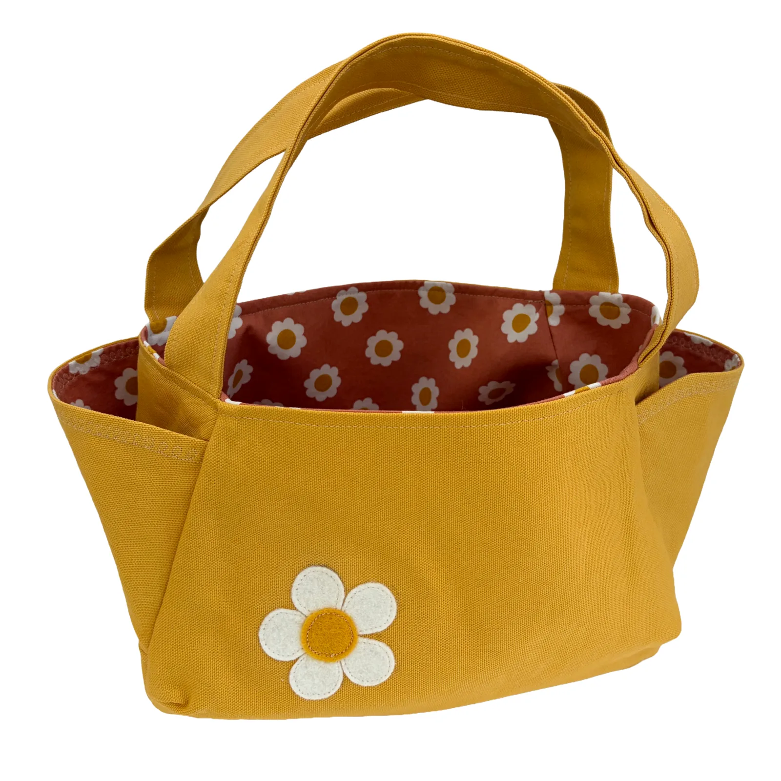 A mustard yellow fabric tote bag with a white and yellow daisy applique on the front and a patterned rust-brown lining visible inside.