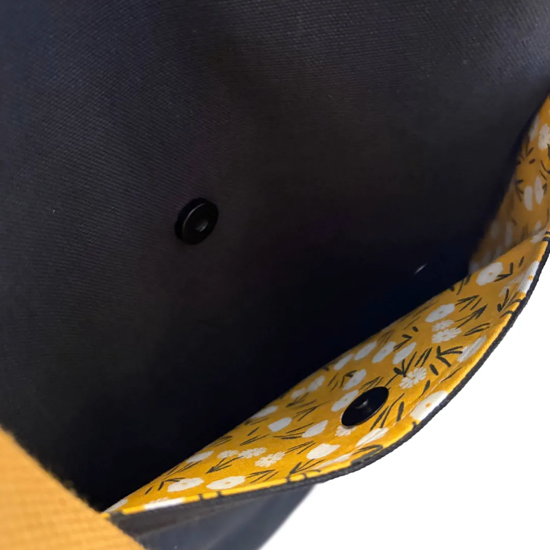 Close-up of a fabric bag or pouch showing a dark navy exterior, a yellow interior lining with a white floral pattern, and black snap buttons.