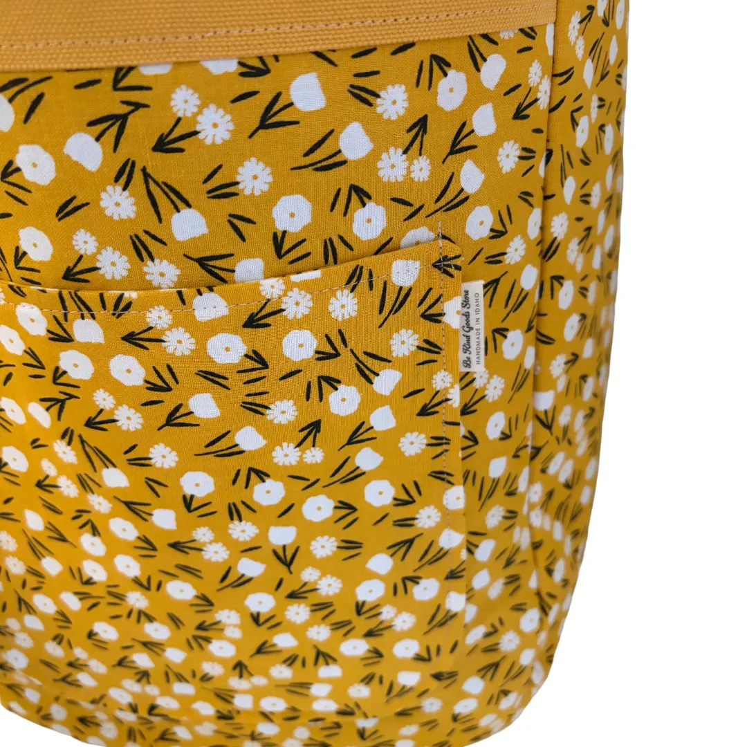 Close-up of a mustard yellow fabric bag with a white and black floral print, showing a side pocket and a small sewn label.