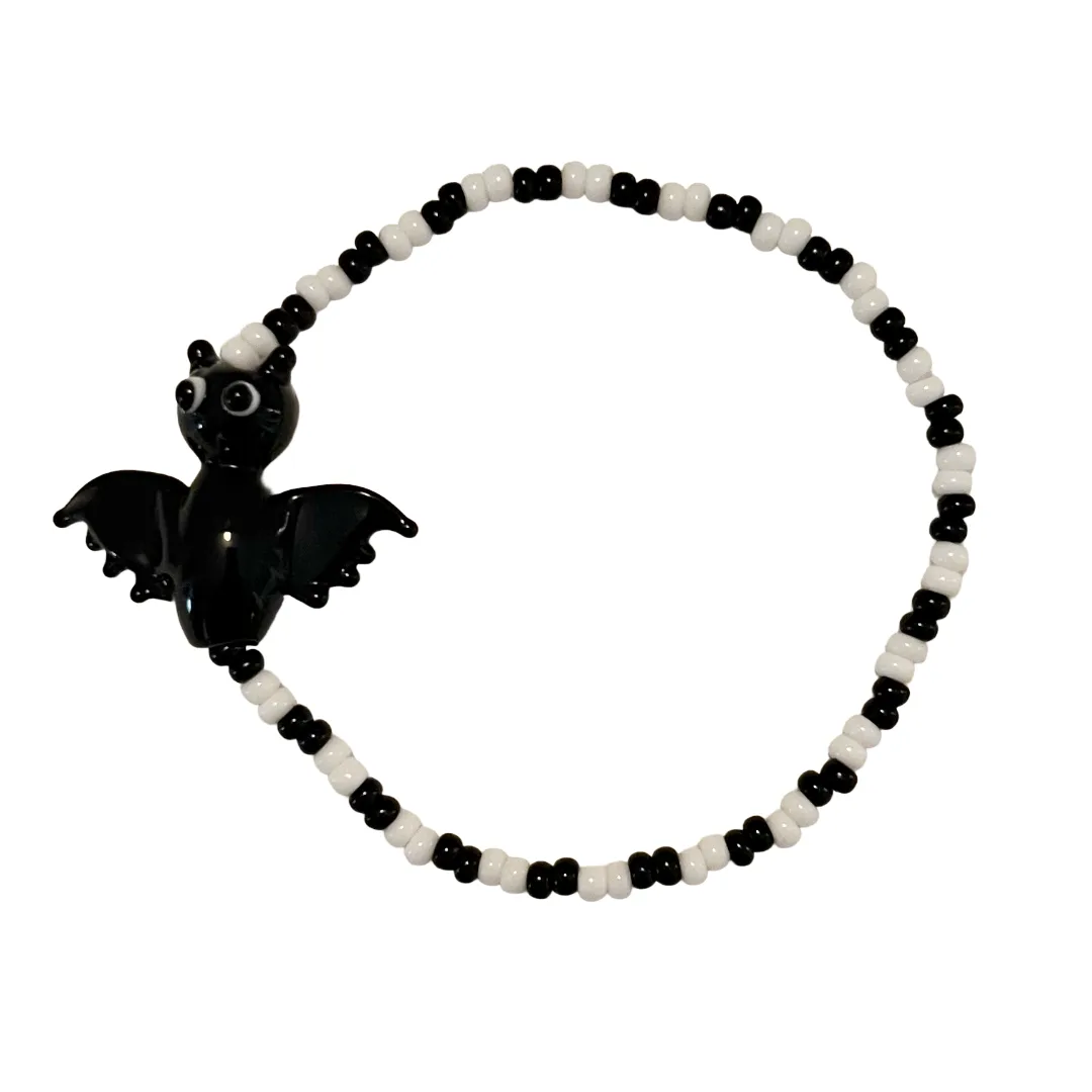 Black bat charm on a black and white beaded bracelet against a white background