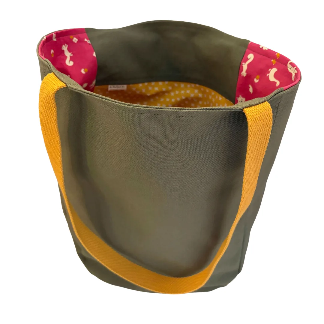 A canvas tote bag with an olive green exterior, mustard yellow webbed handles, and a pink patterned lining with white bunnies and a yellow polka-dot interior.
