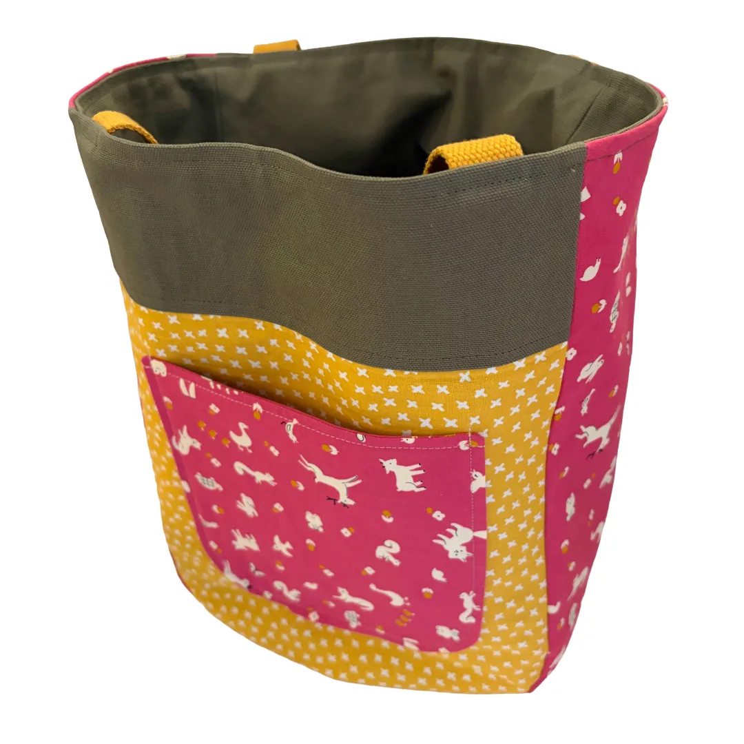 A fabric storage tote bag with a dark olive green upper band, a front pocket in pink fabric with white dog silhouettes, and yellow fabric panels with white stars. The bag is shown on a plain white background.
