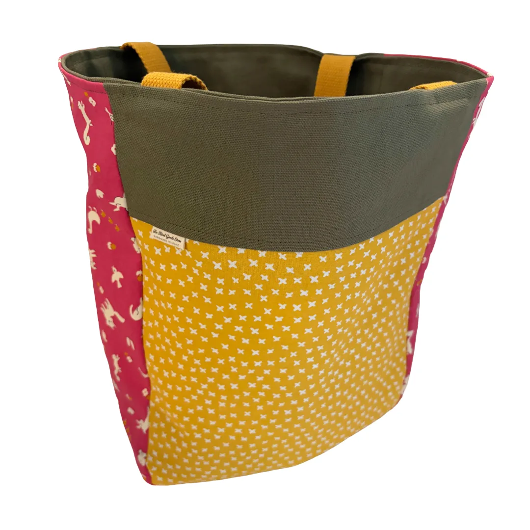 A fabric tote bag with a dark olive green top band, yellow and pink patterned sides, and yellow fabric handles, shown on a plain white background.