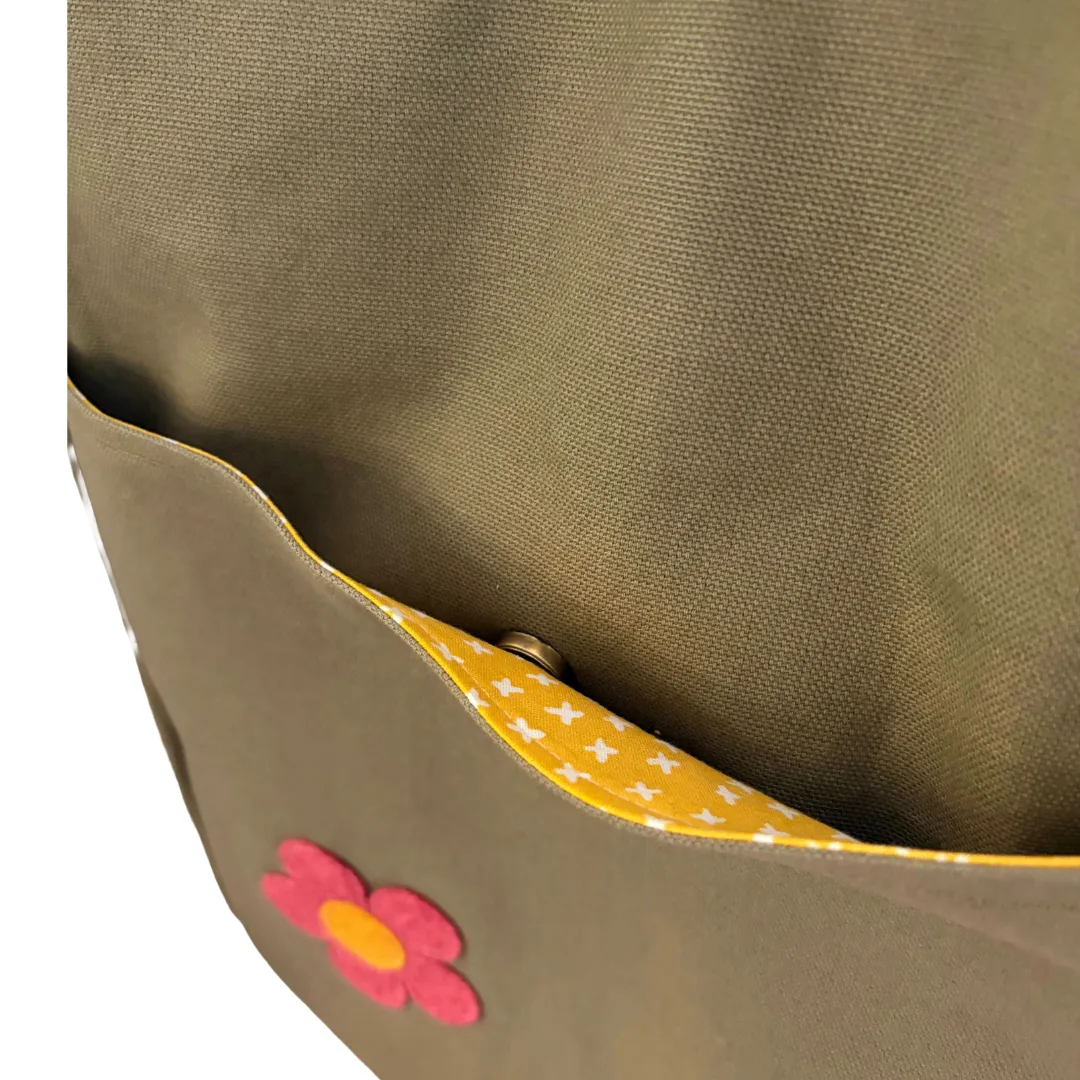 Close-up of an olive fabric bag or pocket with a yellow patterned lining and a pink flower applique.