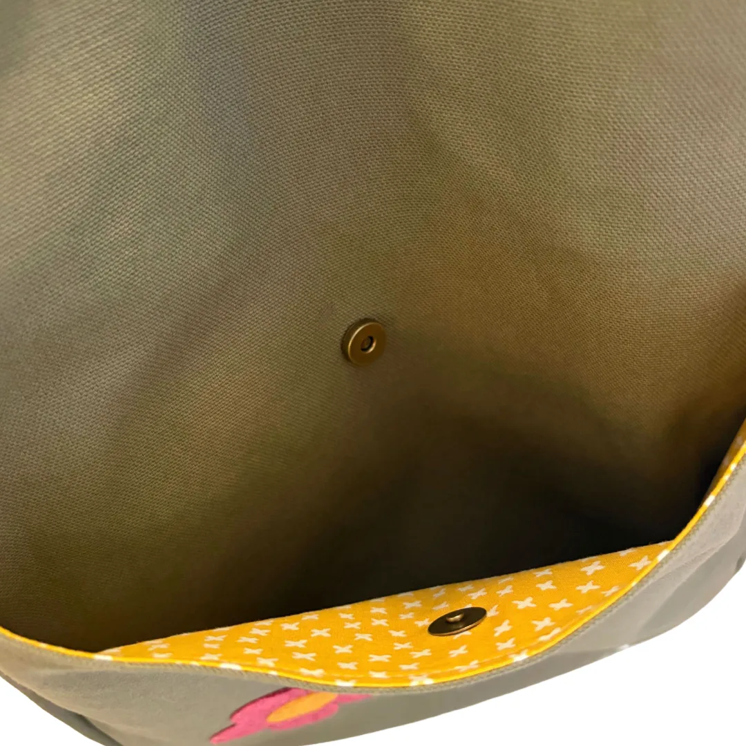 Close-up of the inside of a canvas bag or tote, showing an olive green fabric, a yellow patterned fabric trim with white star print, and brass snap buttons.