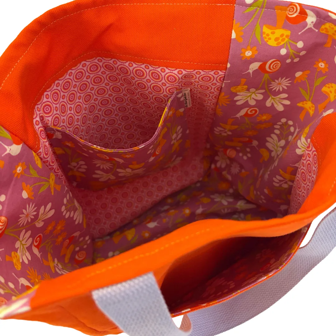 Close-up of a tote bag's interior, featuring a bright orange fabric lining and a pink floral patterned lining with a side pocket.