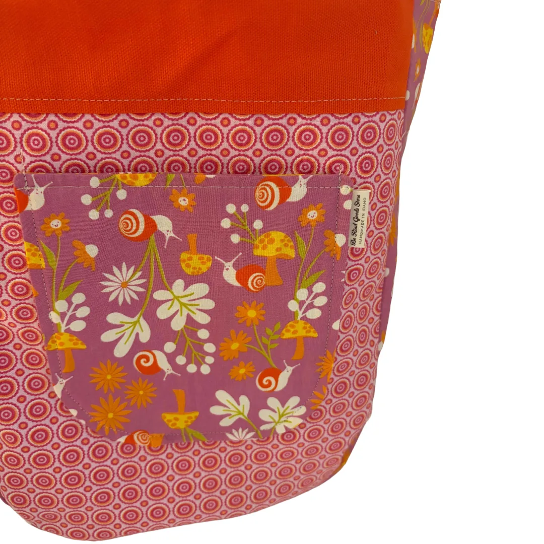 Close-up of a fabric bag or pouch showing a floral front pocket with orange, yellow, white, and pink pattern, plus an orange fabric section above it on a white background.