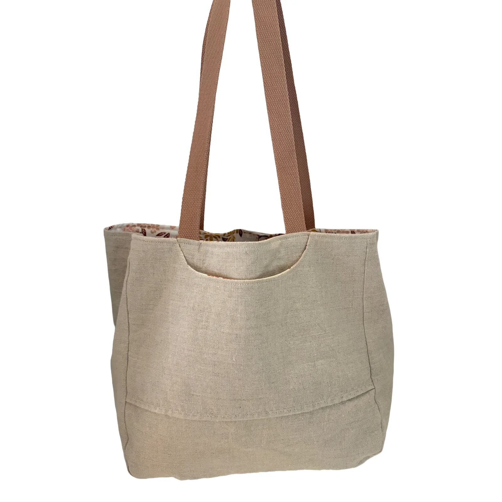 A natural linen tote bag with brown shoulder straps and a floral patterned lining, shown against a plain white background.