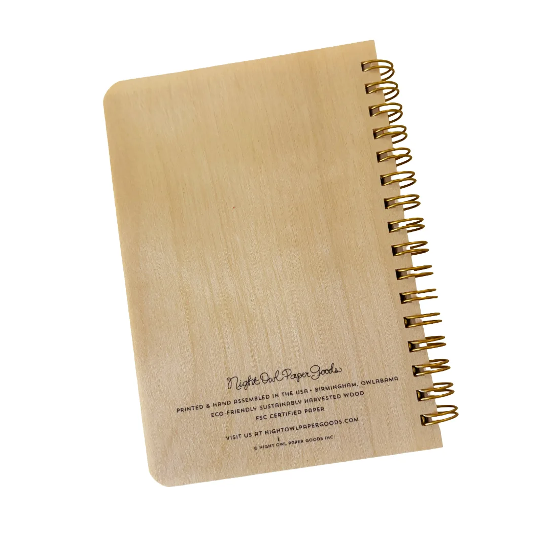 A light natural wood pocket notebook with a gold spiral coil binding, shown on a clean white background. The cover features printed black text at the bottom indicating 'Night Owl Paper Goods' and product details.