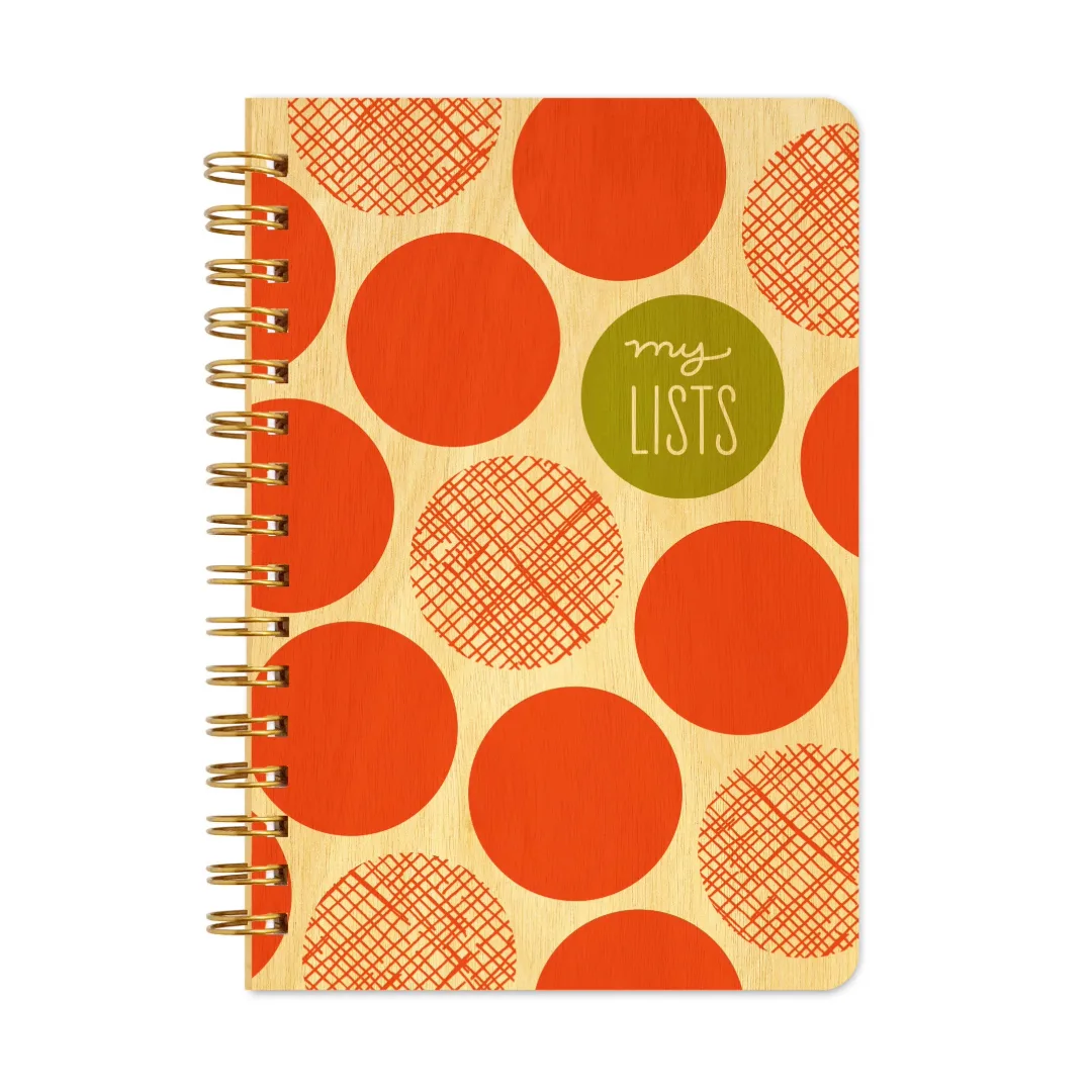 A spiral-bound notebook with a light wood cover decorated with large orange and red polka dots, some filled and some cross-hatched. A green circular sticker on the cover reads 'my LISTS' in white script.