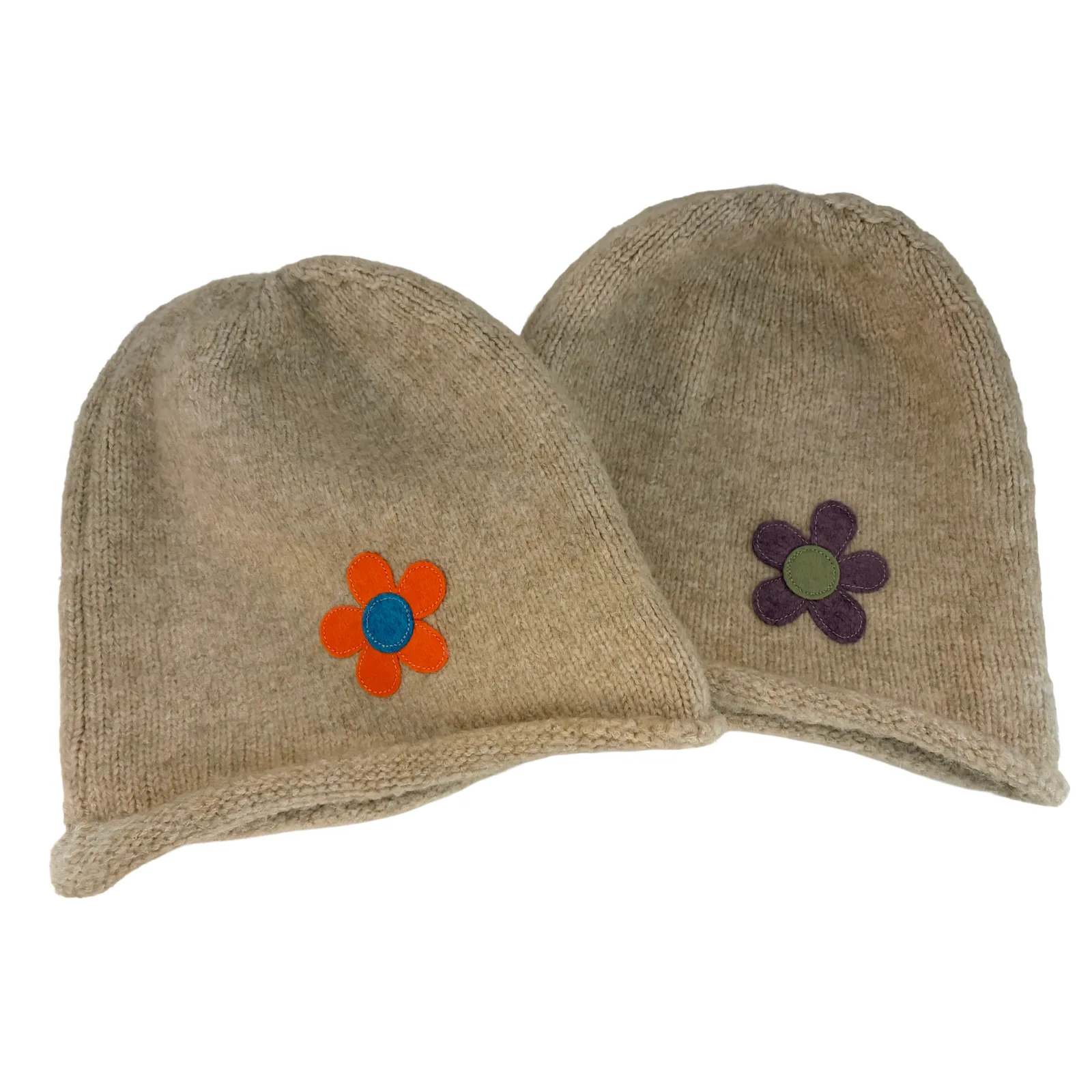 Two beige knit beanie hats on a white background, each decorated with a small felt flower applique. The hat on the left has an orange flower with a blue center, and the hat on the right has a purple flower with a green center.