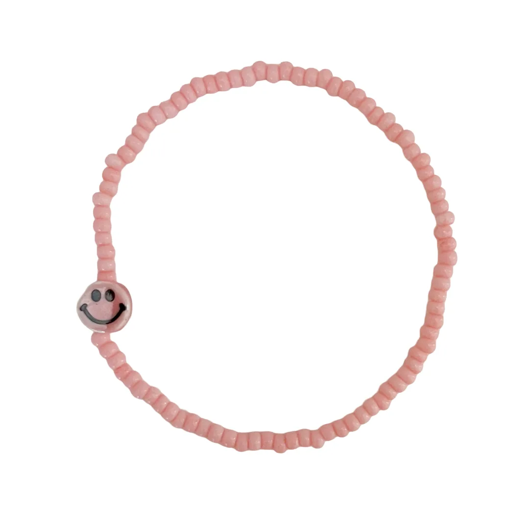Pink beaded bracelet with a smiley face charm on a white background