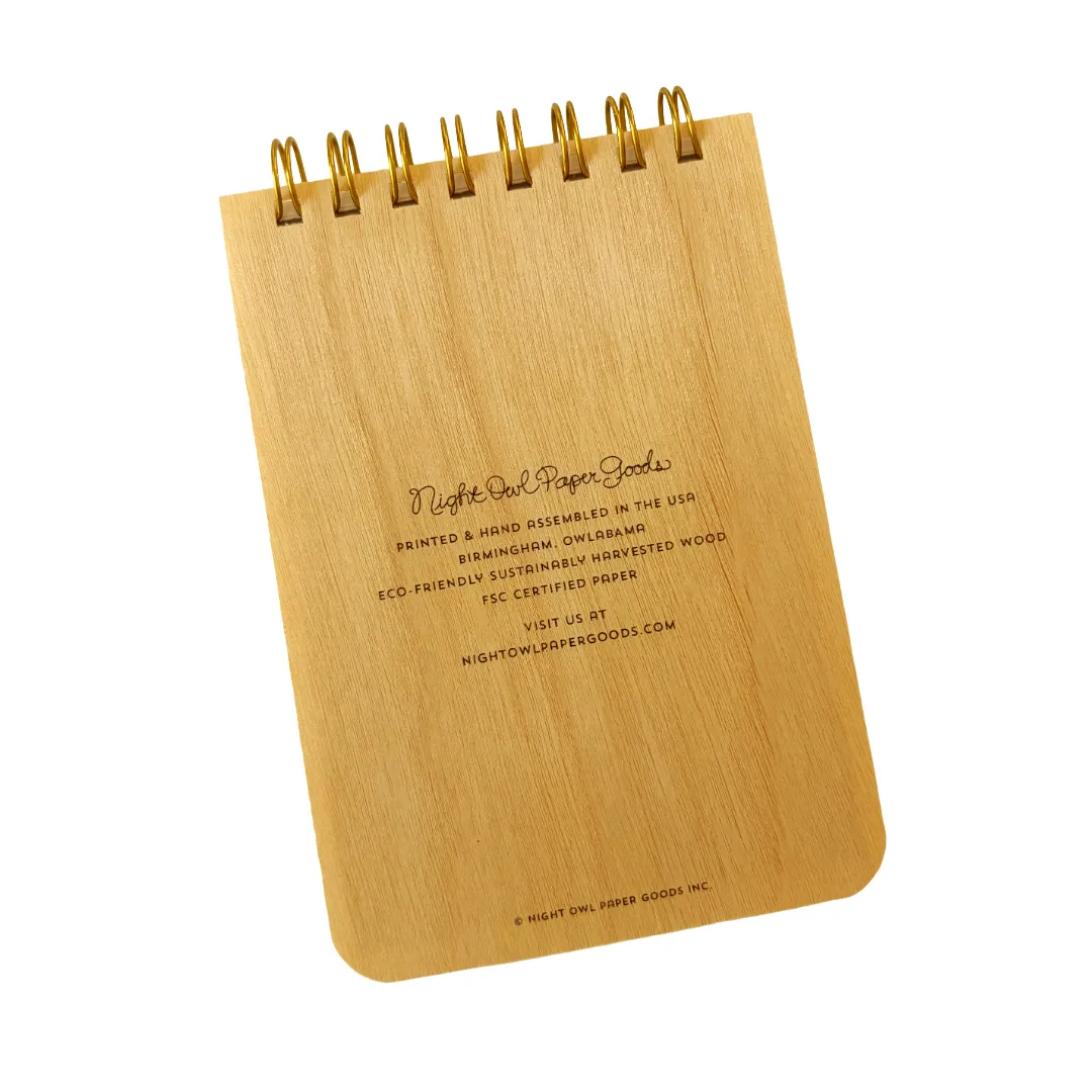 A small spiral-bound notebook made from natural wood with gold wire binding, shown on a plain white background. The front has printed black text reading Night Owl Paper Goods.
