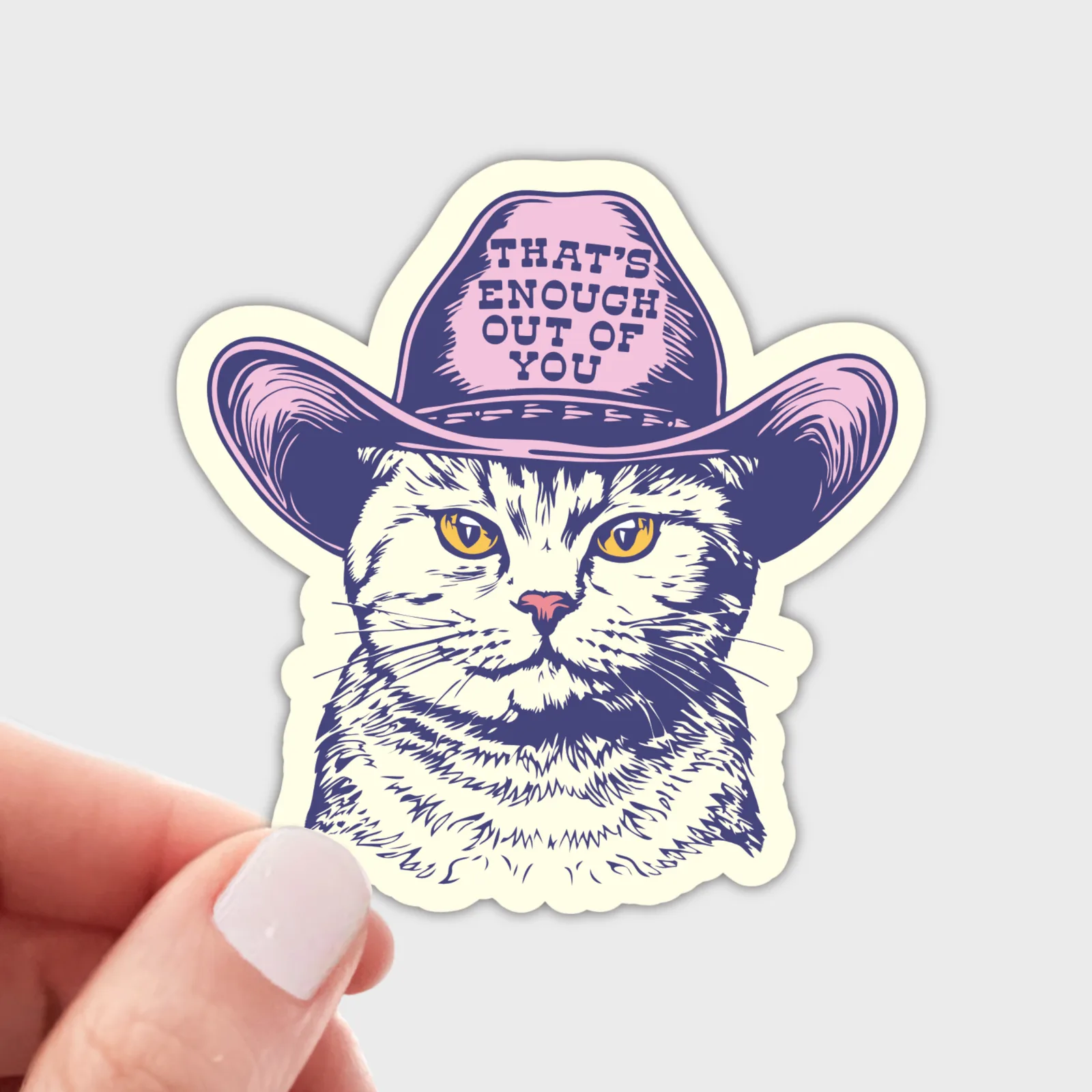 Sticker of a cat wearing a cowboy hat with text, held by a hand on a light gray background