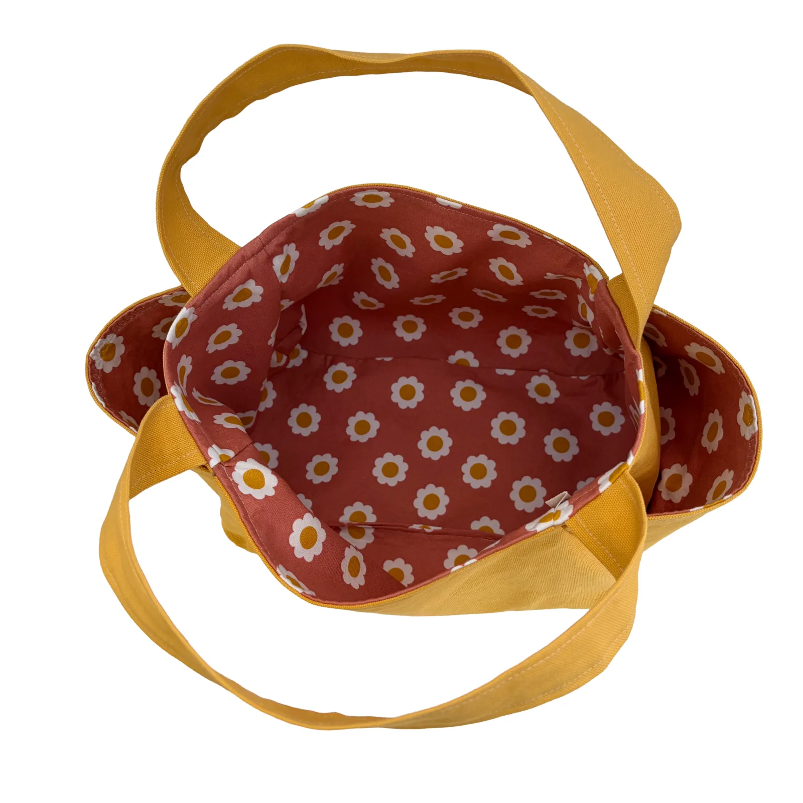 A mustard yellow fabric tote bag shown from above, with a rust-red patterned lining featuring a white and yellow daisy print.