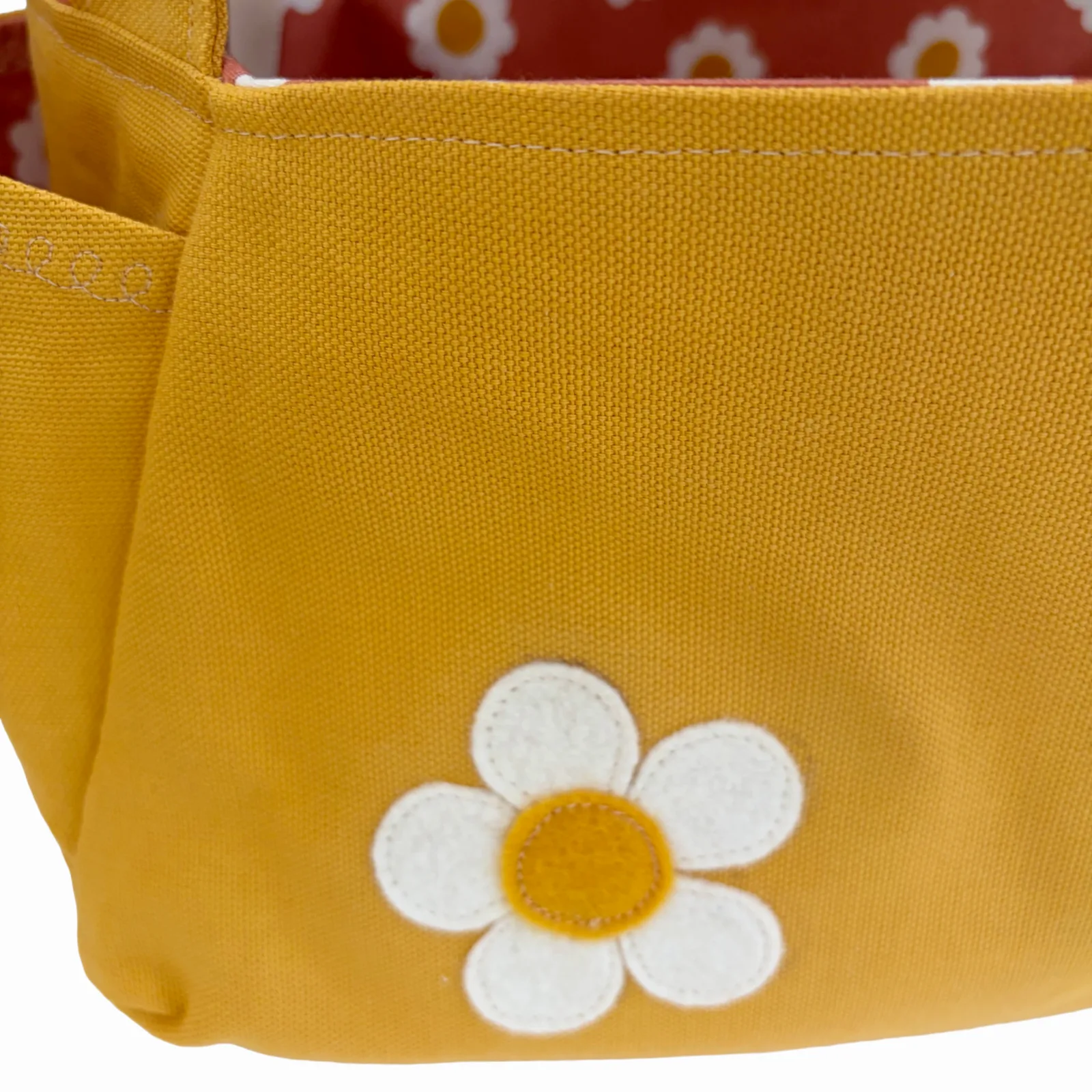 Close-up of a mustard yellow fabric pouch featuring a white felt daisy applique with a yellow center on the front.